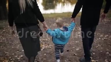 年轻的幸福夫妇在秋天公园散步。 一位年轻的母亲和年轻的父亲牵着小男孩，一起走进来